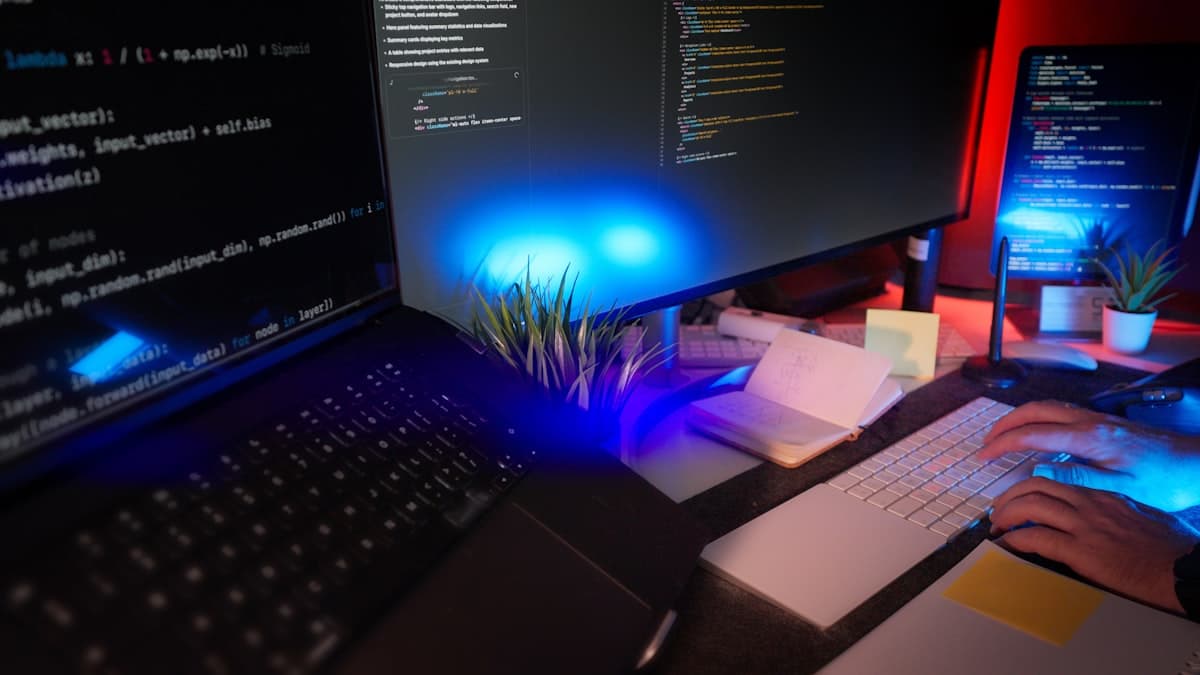 Programador trabalhando em ambiente de desenvolvimento com múltiplos monitores exibindo código